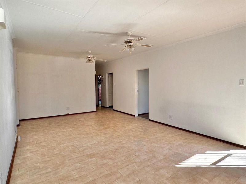A spacious, empty living area featuring neutral tiled flooring, dual ceiling fans, and access to adjoining rooms.