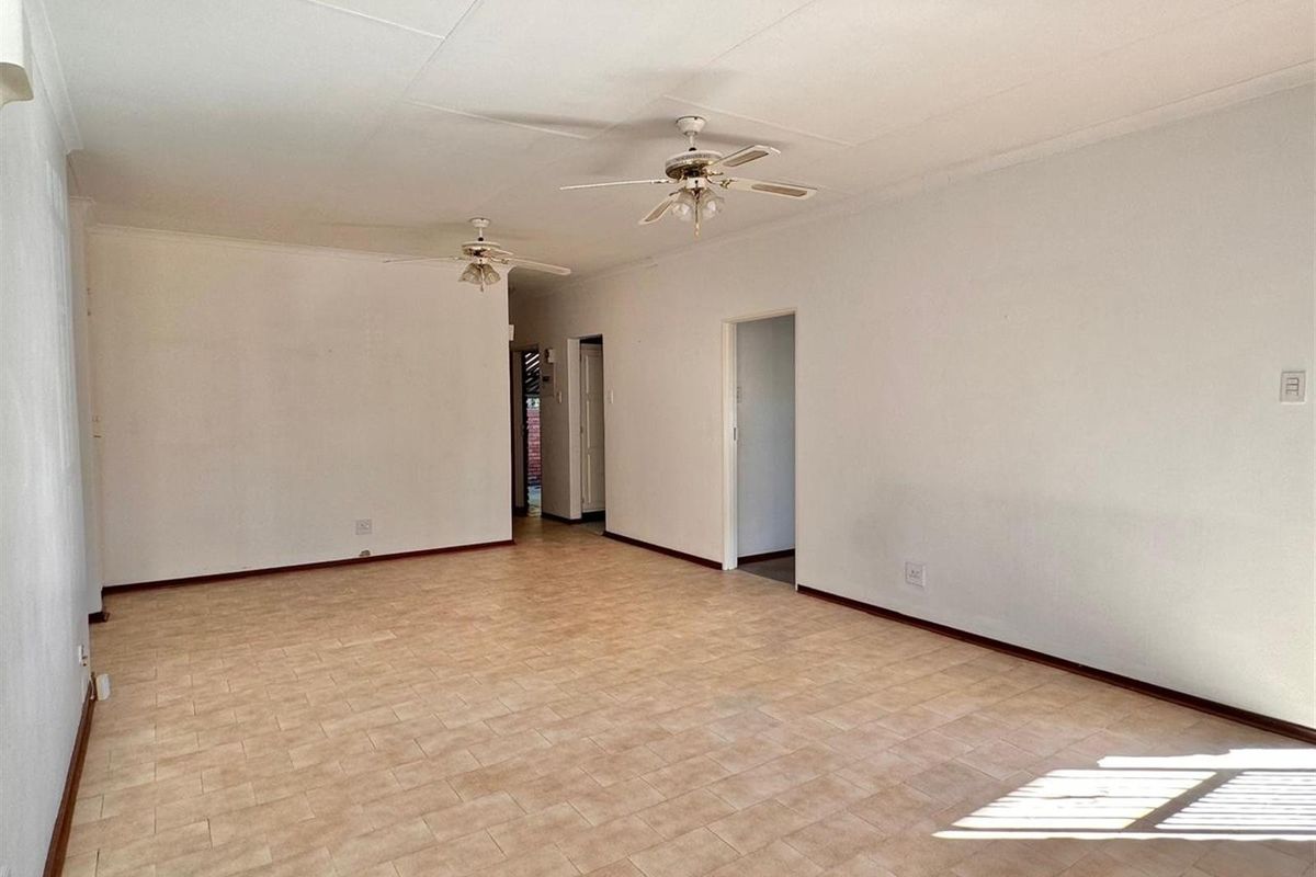 A spacious, empty living area featuring neutral tiled flooring, dual ceiling fans, and access to adjoining rooms.
