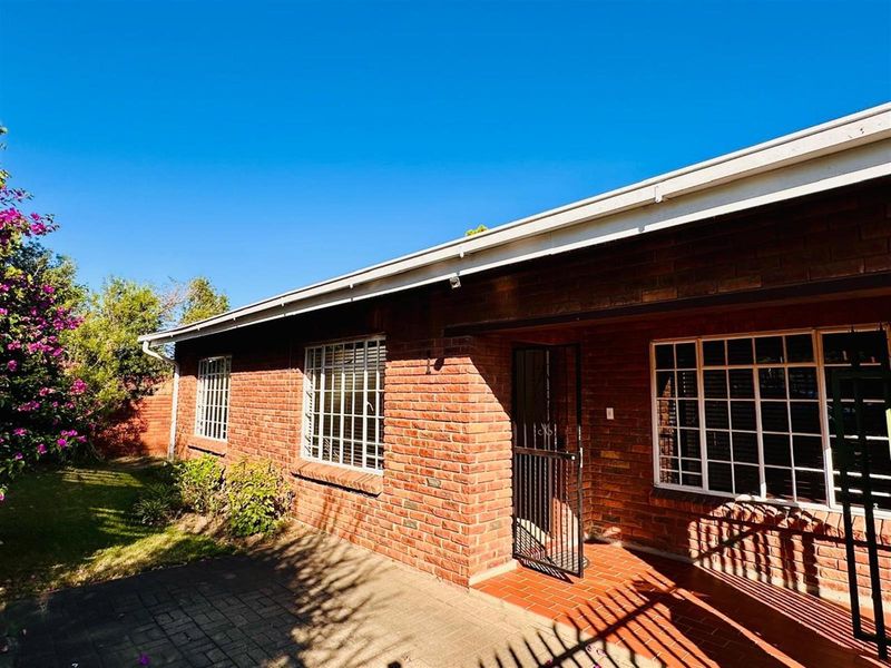 A view of the rear exterior of the townhouse, featuring classic red brick facade, white-framed windows with security bars, and a paved patio area.