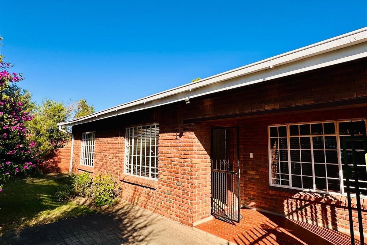 A view of the rear exterior of the townhouse, featuring classic red brick facade, white-framed windows with security bars, and a paved patio area.