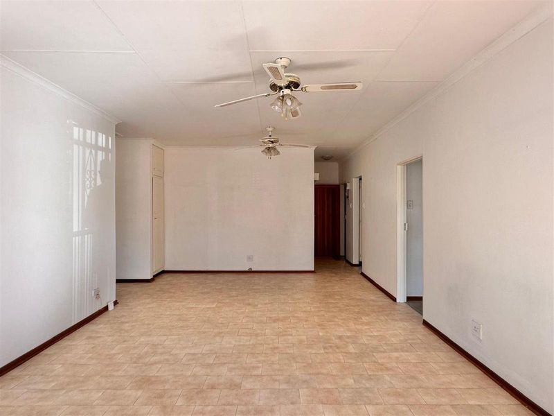 A spacious, empty living area featuring tiled flooring, dual ceiling fans, and built-in storage cupboards, offering a blank canvas for personalization.