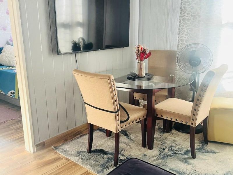 A dining area featuring wood-paneled walls and wood-look flooring, with a view into an adjacent bedroom.