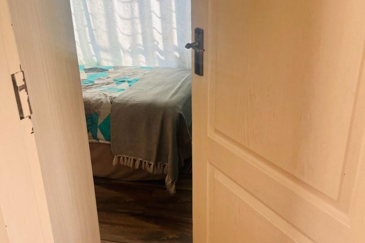 A view through a doorway into a bedroom featuring wood-look flooring and natural light filtering through window coverings.