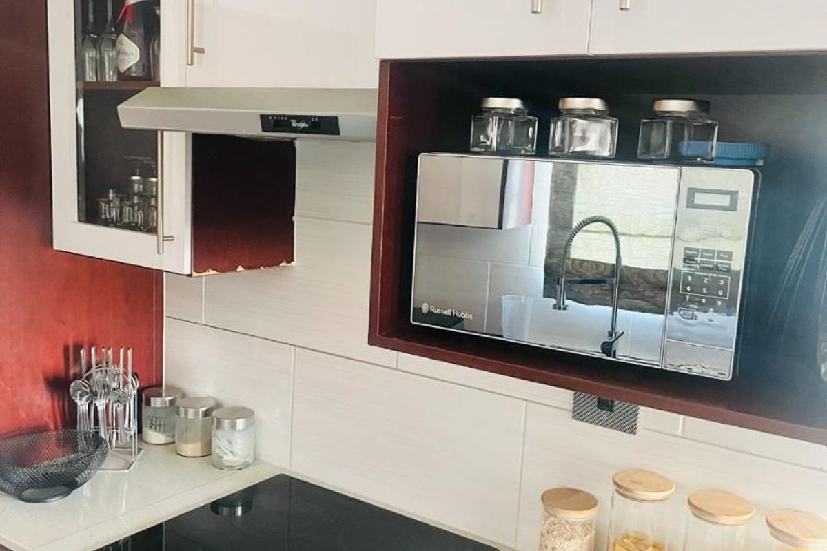 Modern kitchen featuring white and dark cabinetry, a built-in electric hob, oven, extractor fan, and a dedicated microwave nook with stone-look countertops.