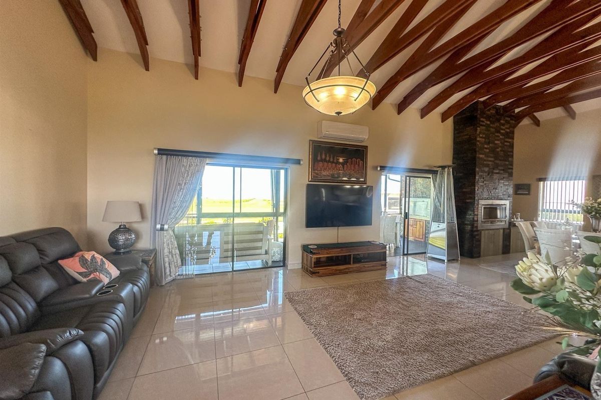 Spacious living room featuring high vaulted ceilings with exposed timber beams, polished tiled floors, and a prominent built-in brick fireplace.