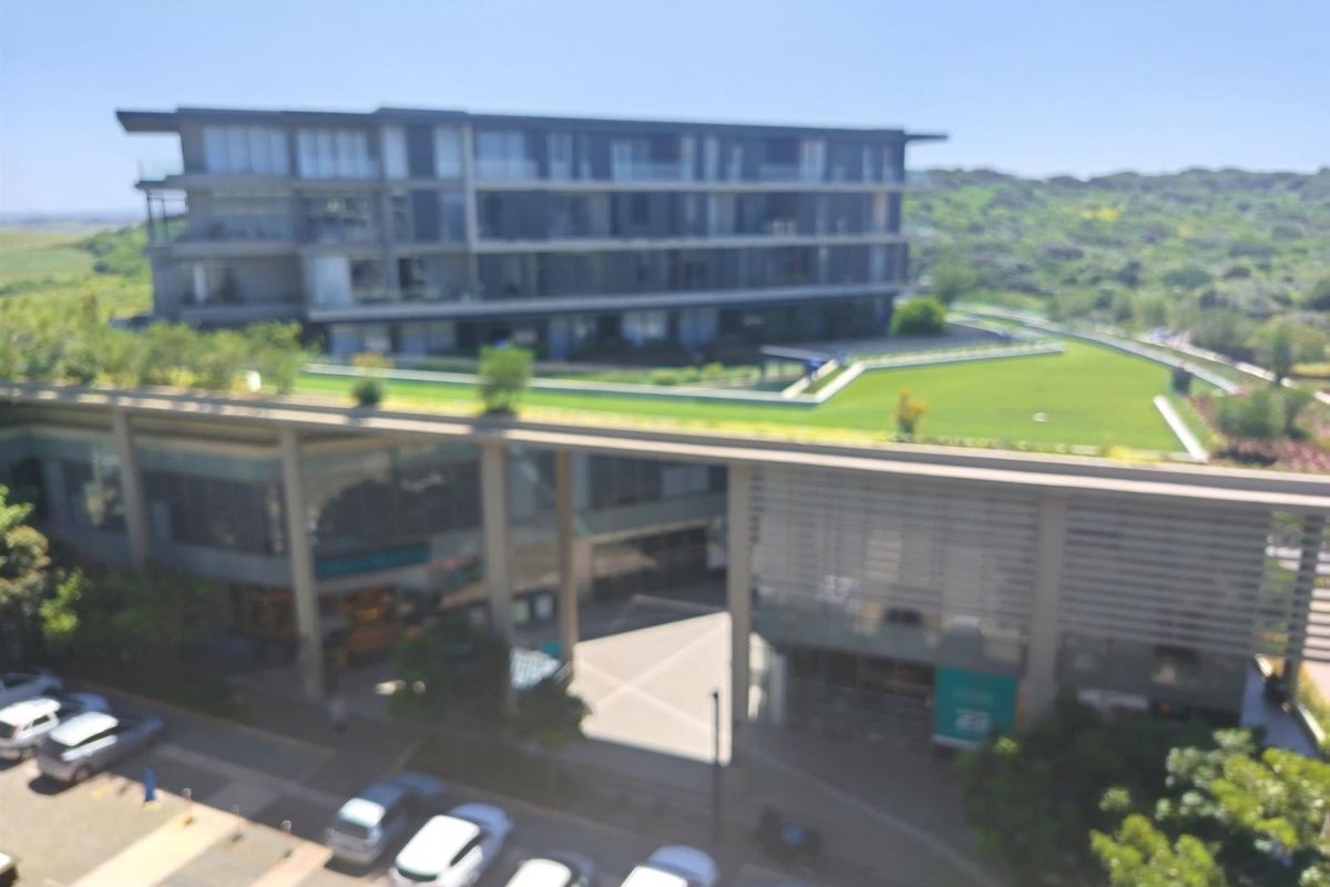 An elevated aerial view of a modern apartment complex featuring landscaped green roof areas and surrounding parking facilities.