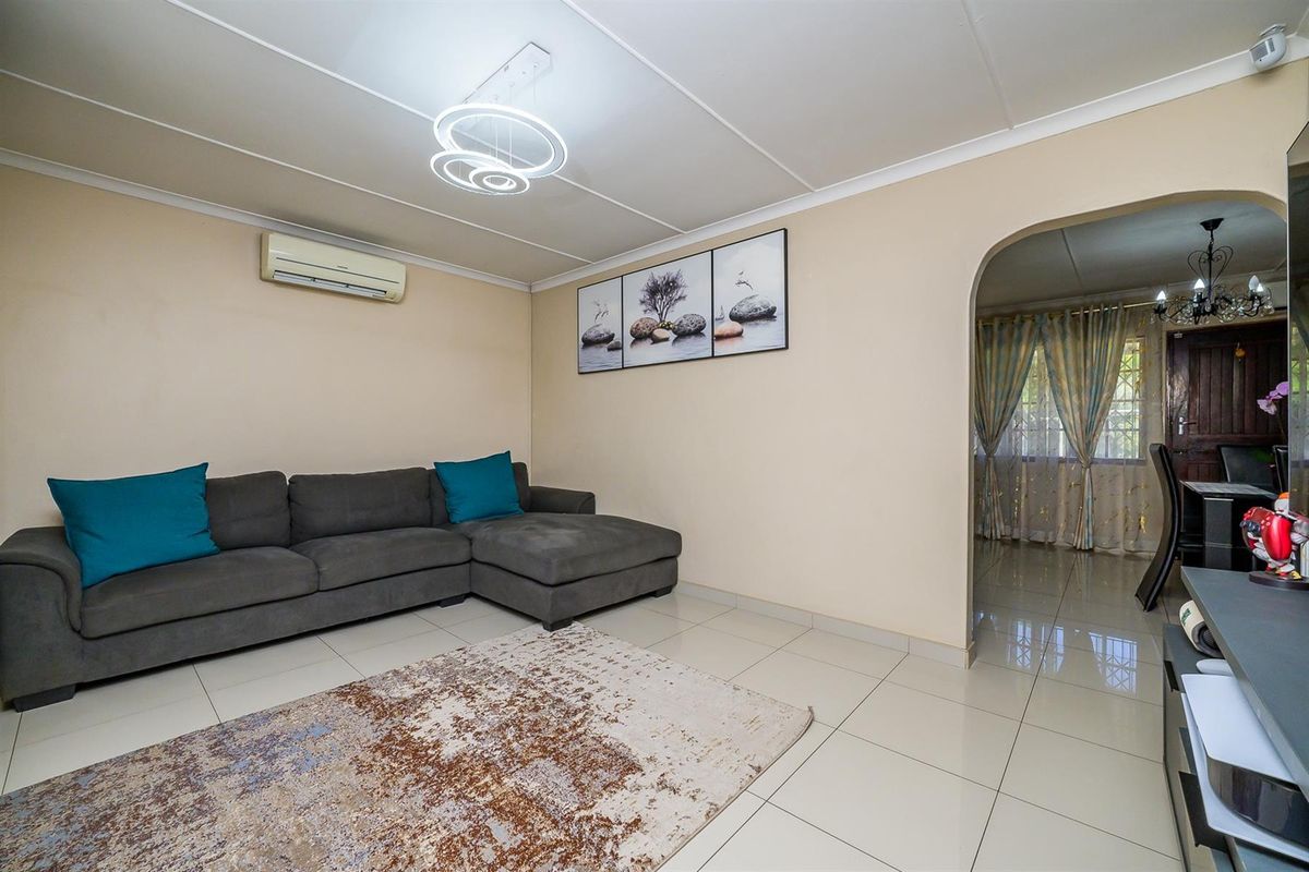 A living room featuring tiled flooring, a wall-mounted air conditioning unit, and an arched doorway leading to an adjacent dining area.