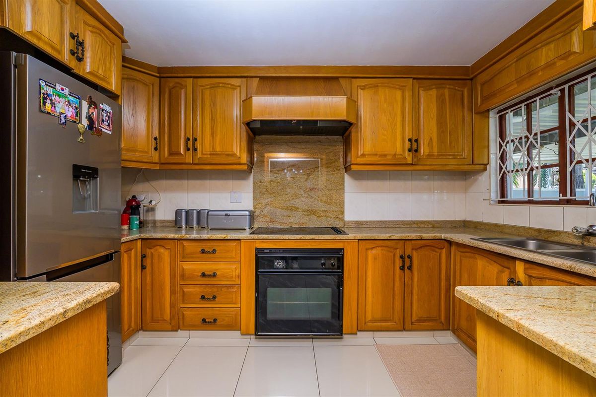 A functional kitchen featuring traditional timber cabinetry, granite countertops, a built-in oven, and a hob with an integrated extractor fan.