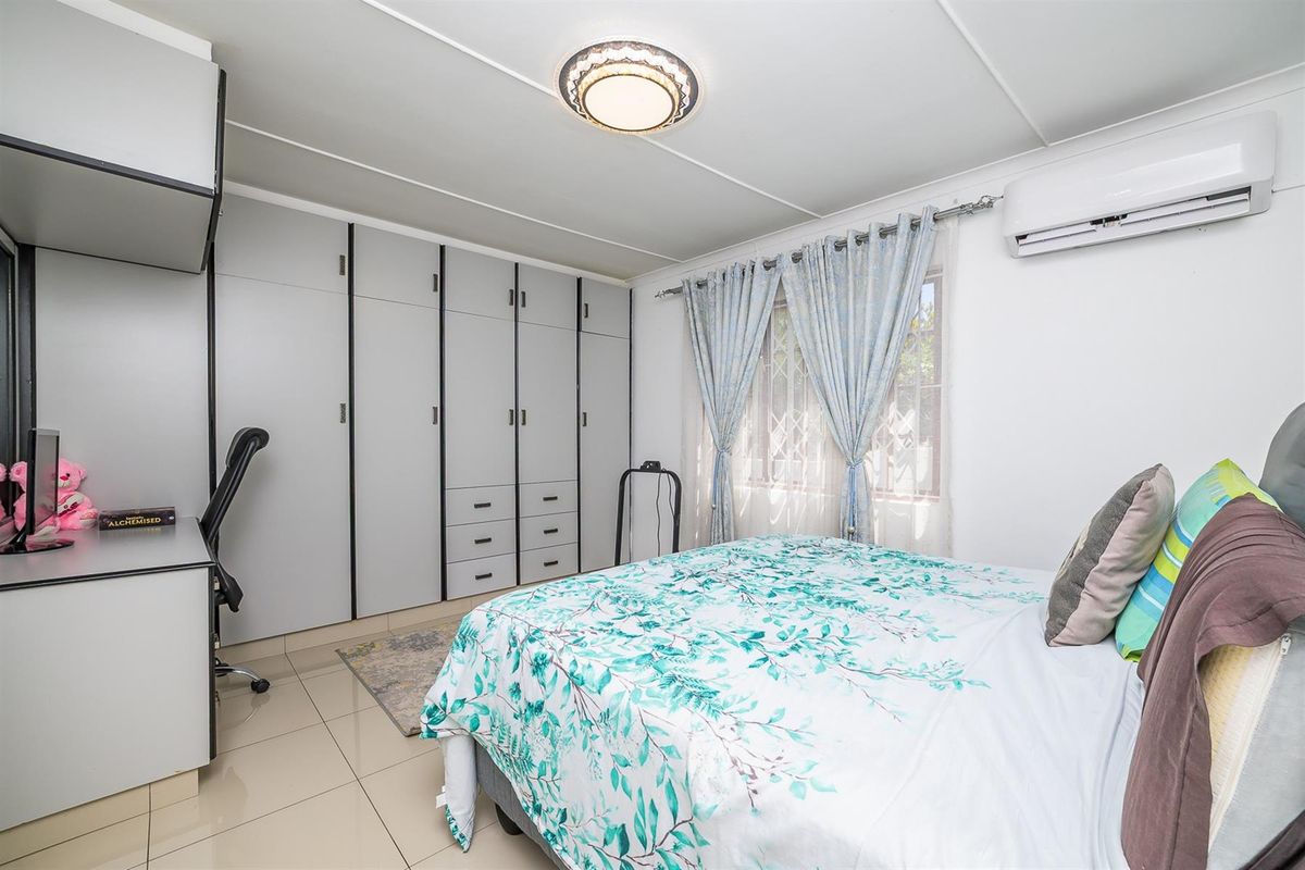 A well-lit bedroom featuring built-in cupboards, tiled flooring, and a wall-mounted air conditioning unit.