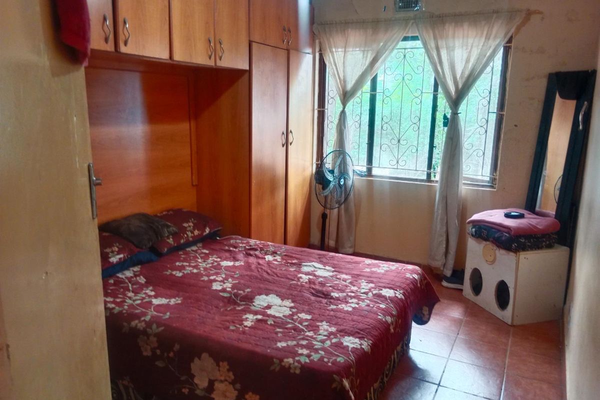 A bedroom featuring built-in wooden cabinetry and tiled flooring, with a window protected by security bars.