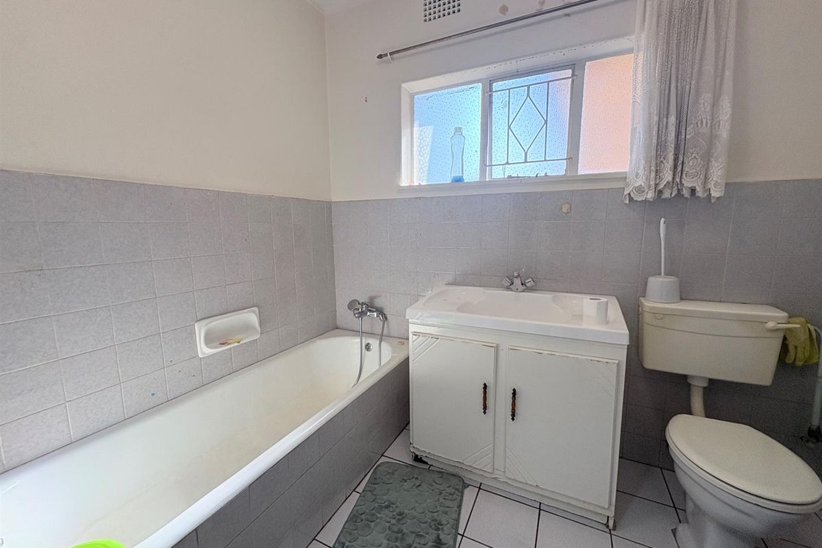 A dated bathroom featuring a standard bathtub, vanity basin, and toilet with tiled walls and flooring.