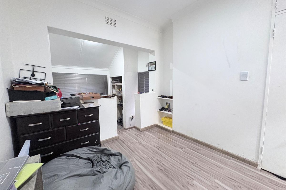A versatile bedroom space featuring laminate flooring, built-in shelving, and an adjoining alcove area with natural light.