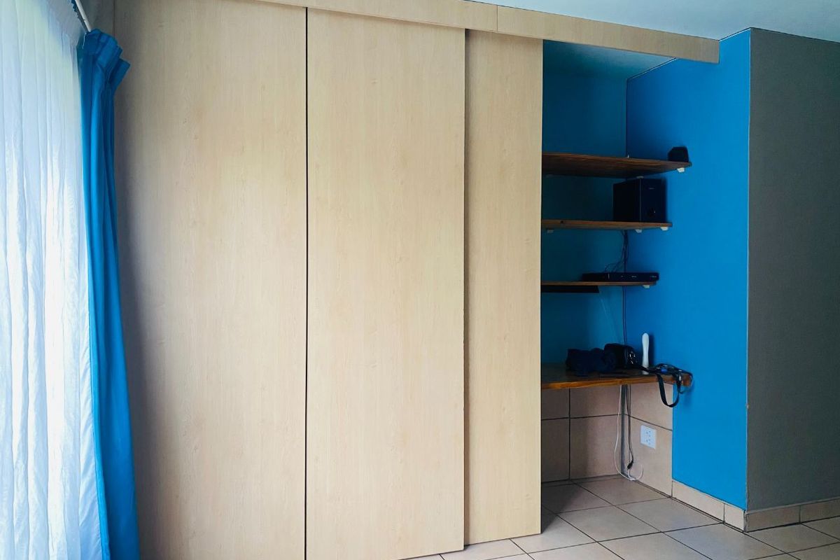 Bedroom featuring built-in light wood sliding door wardrobes and an integrated open shelving unit with a desk area.