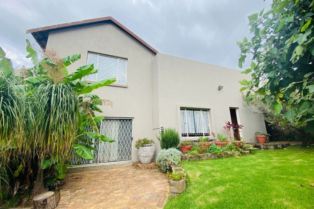 Rear view of the house featuring a paved patio area, landscaped garden, and security gates on the sliding doors.