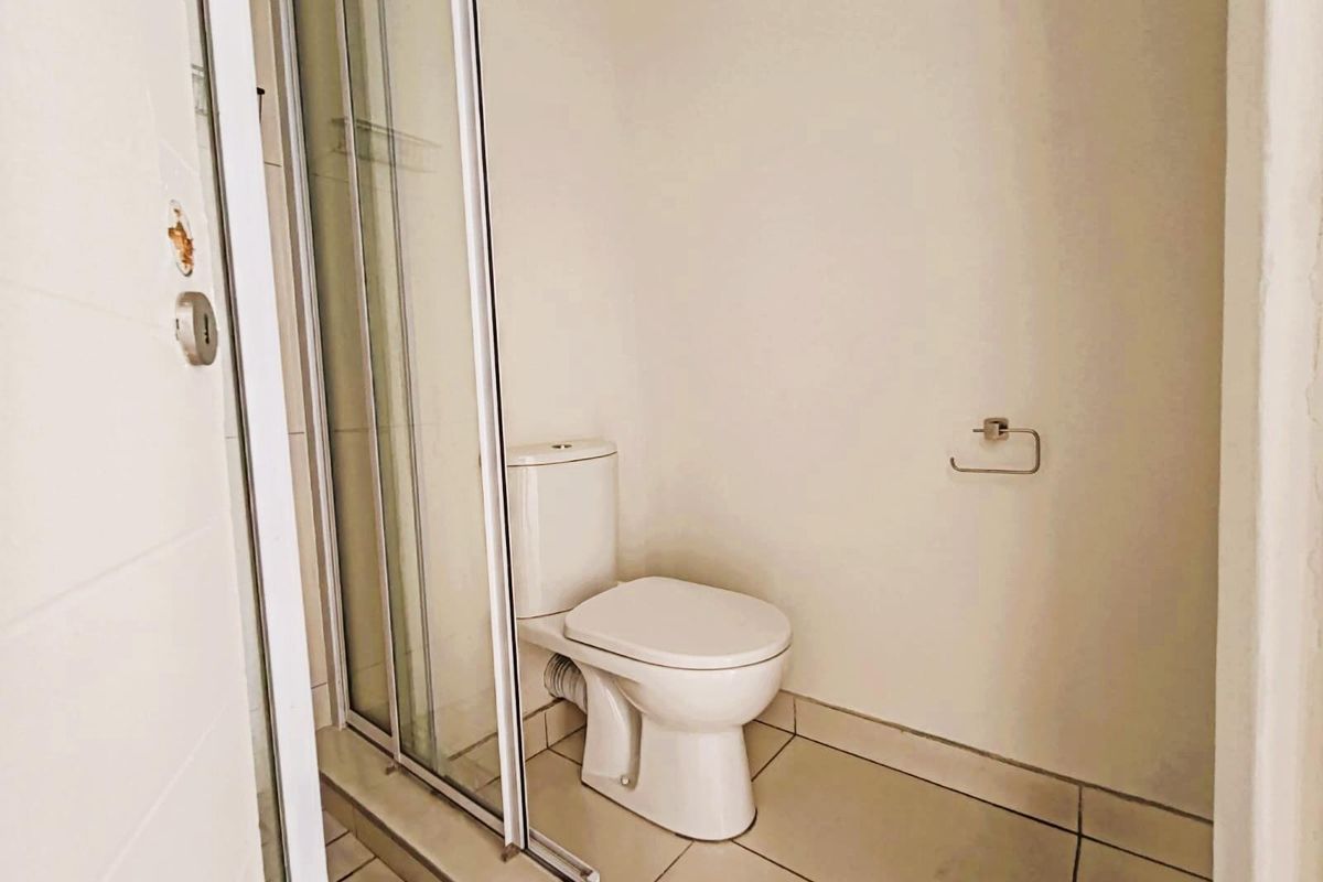 A functional bathroom featuring a tiled floor, a standard white toilet, and a glass-enclosed shower stall.