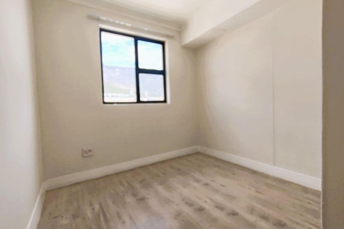 A bright, empty bedroom featuring neutral walls, light wood-look flooring, and a window with a view.