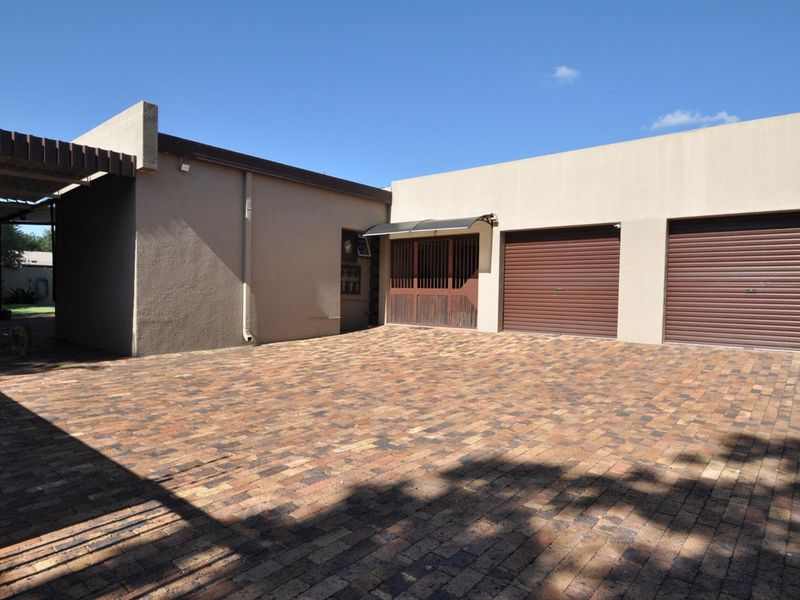 Exterior view of the property featuring a paved driveway, double garage with roller doors, and a covered patio area.