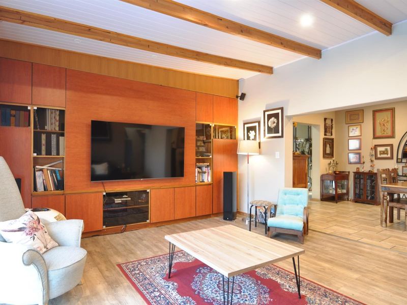 Spacious open-plan living area featuring exposed timber ceiling beams, wood-look flooring, and a large built-in timber cabinetry unit with integrated shelving.