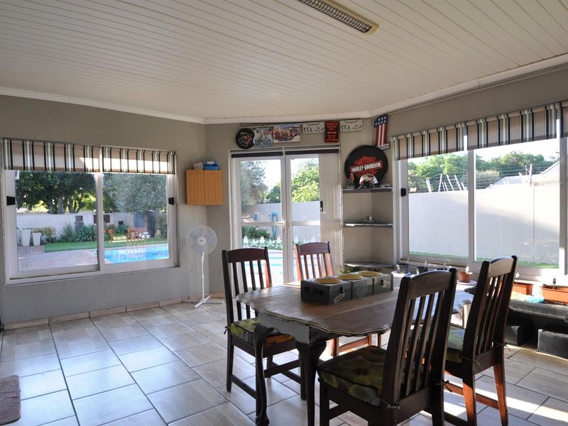 A bright, tiled patio area featuring large windows and glass sliding doors that provide direct access and views to the outdoor pool and garden.