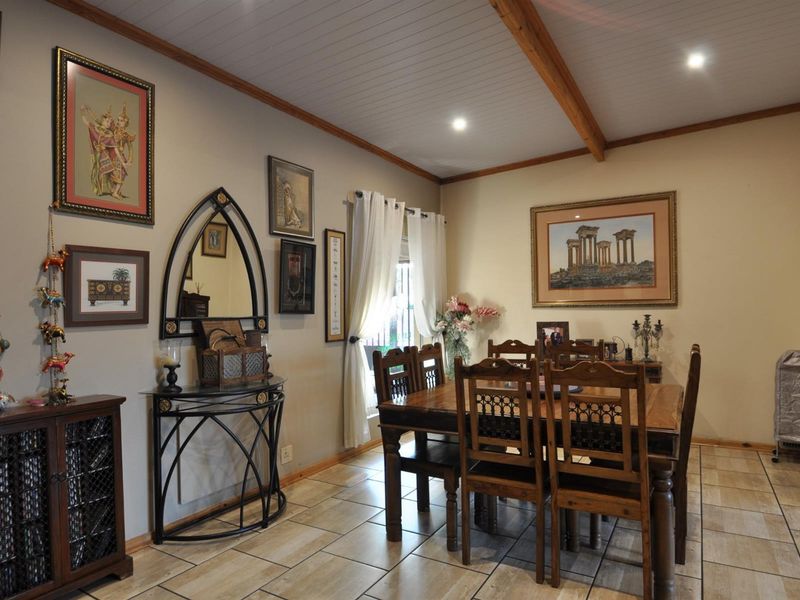 A dining room featuring tiled flooring, a white paneled ceiling with exposed timber beams, and recessed downlighting.