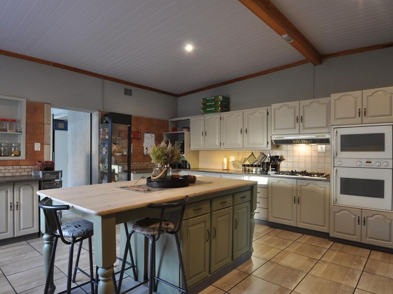 Spacious kitchen featuring a central island, built-in oven, gas hob, extractor fan, and ample cabinetry, finished with tiled flooring and a timber-accented ceiling.