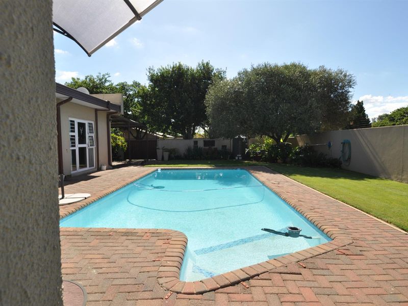 A well-maintained outdoor pool area featuring a paved surround, manicured lawn, and perimeter walling, providing a private space for relaxation and recreation.