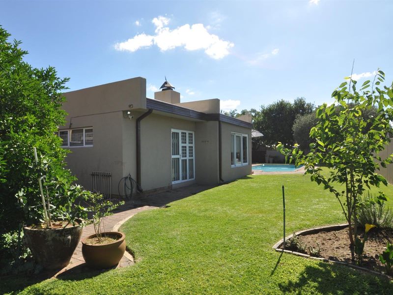 Rear view of the property featuring a landscaped garden, paved walkway, and a swimming pool in the background.