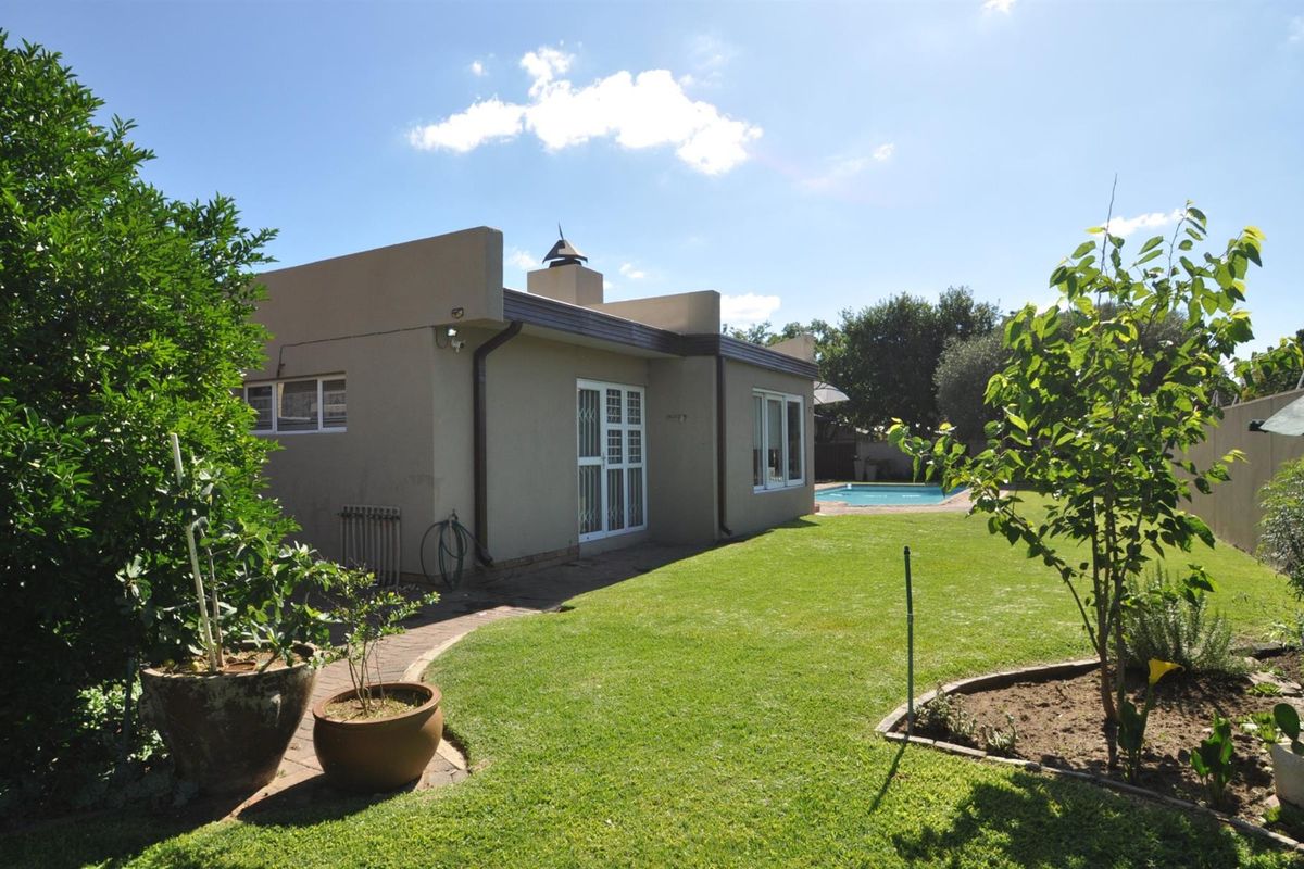 Rear view of the property featuring a landscaped garden, paved walkway, and a swimming pool in the background.