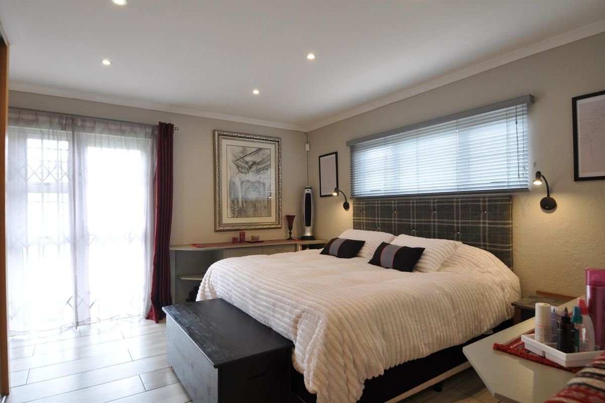 A well-maintained bedroom featuring tiled flooring, recessed ceiling lighting, a built-in headboard, and direct access to an outdoor area via a glass door.