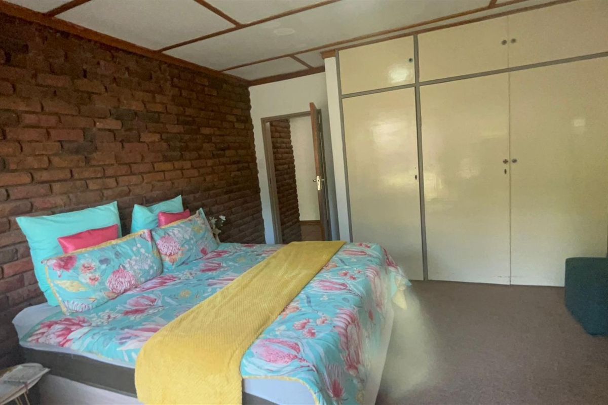 Bedroom featuring an exposed brick feature wall, built-in cupboards, and exposed beam ceiling.