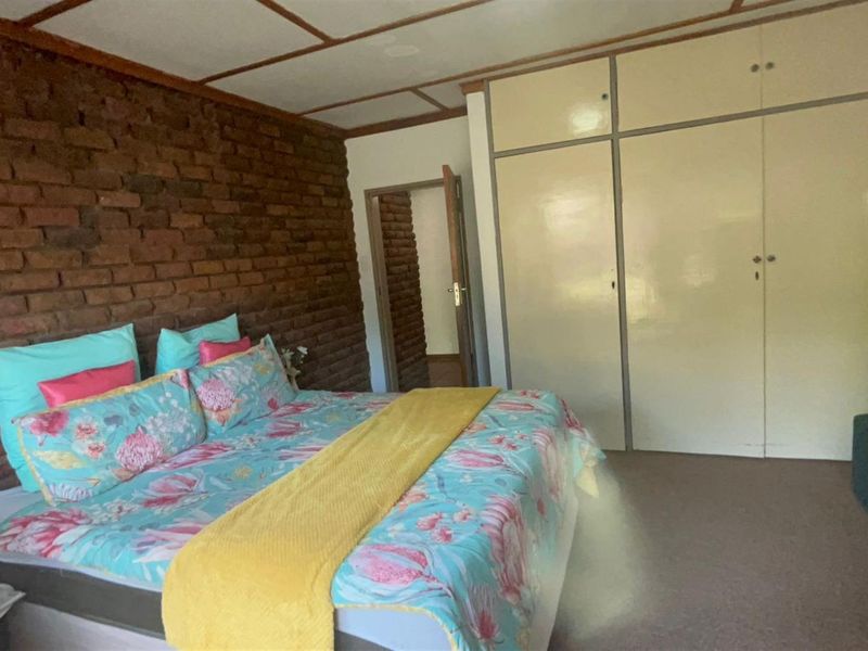 Bedroom featuring an exposed brick feature wall, built-in cupboards, and exposed beam ceiling.