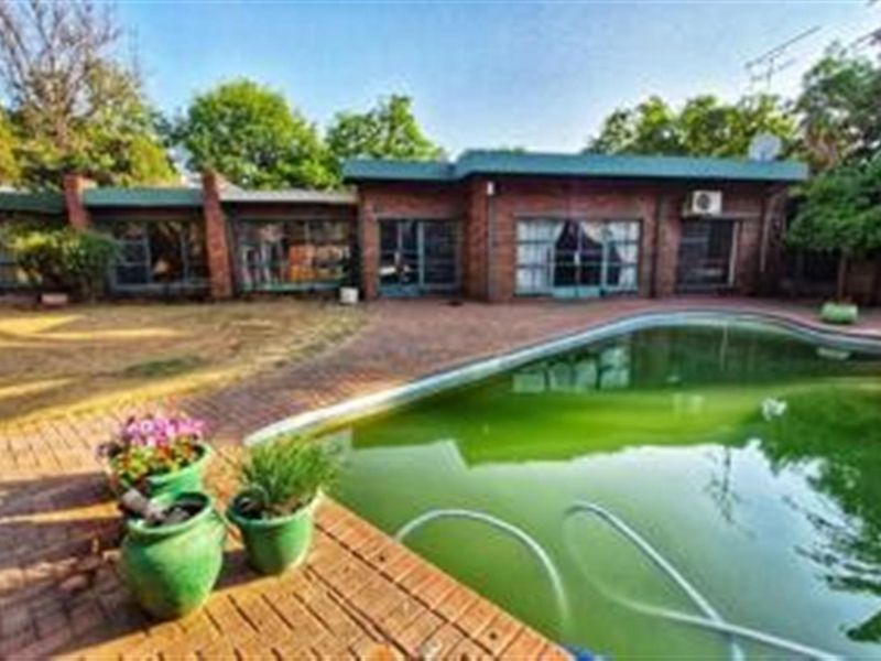 Rear exterior view featuring a brick-faced house with sliding glass doors opening onto a paved patio area and a swimming pool.