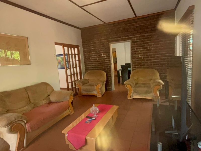 A living room featuring an exposed brick wall, tiled flooring, and timber ceiling beams, providing a rustic foundation for potential interior updates.