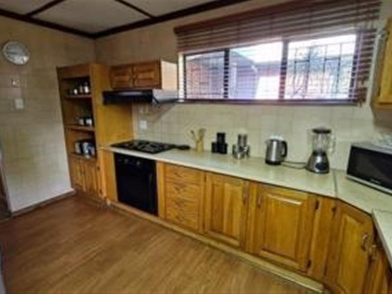 A functional kitchen featuring wooden cabinetry, laminate countertops, a built-in oven, and a gas hob with a tiled splashback.