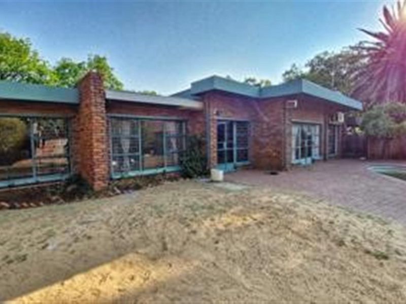 Rear view of a brick house featuring a paved patio area, large windows, and an adjacent swimming pool set in a garden.