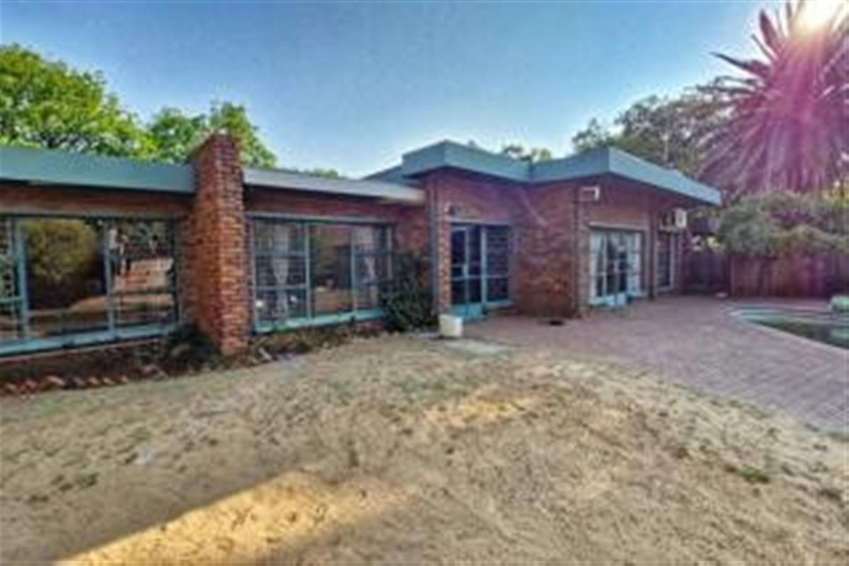 Rear view of a brick house featuring a paved patio area, large windows, and an adjacent swimming pool set in a garden.
