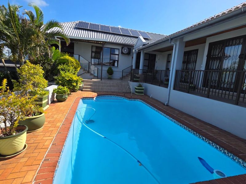 Outdoor pool area featuring a paved deck, solar panels on the roof, and a covered patio space.
