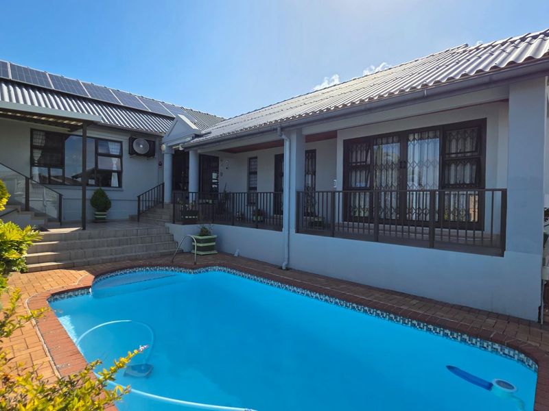 A well-maintained rear exterior view featuring a swimming pool, paved patio area, and a house with solar panels and security gates.