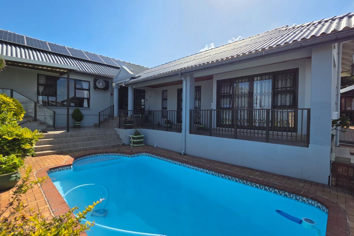 A well-maintained rear exterior view featuring a swimming pool, paved patio area, and a house with solar panels and security gates.