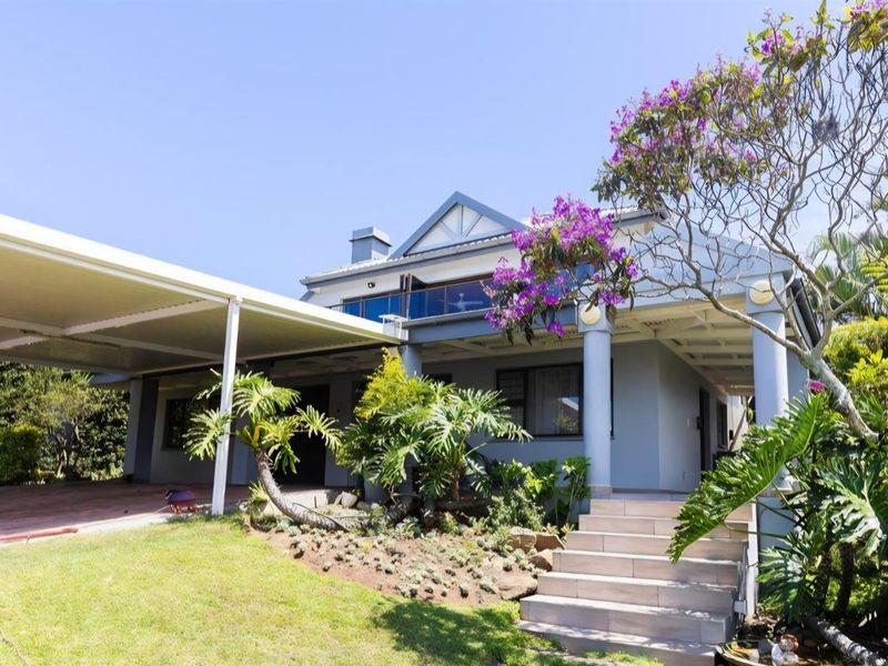 A well-maintained residential property featuring a covered carport, paved entrance steps, and a landscaped front garden with established trees and shrubs.