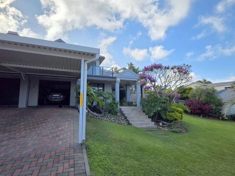 Front exterior view featuring a paved driveway, covered carport, landscaped garden, and a raised entrance with stairs leading to the main dwelling.