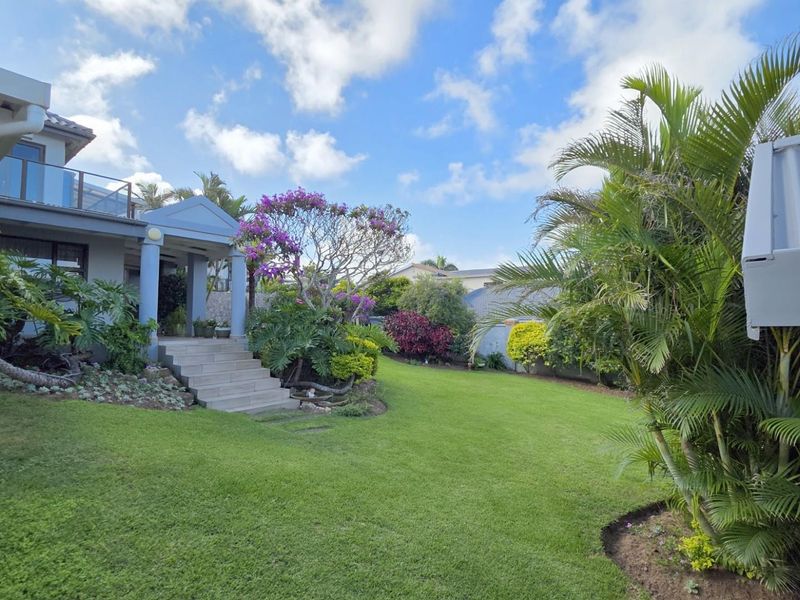 A well-maintained rear garden featuring a lush lawn, mature landscaping, and a paved staircase leading to the elevated patio area of the house.