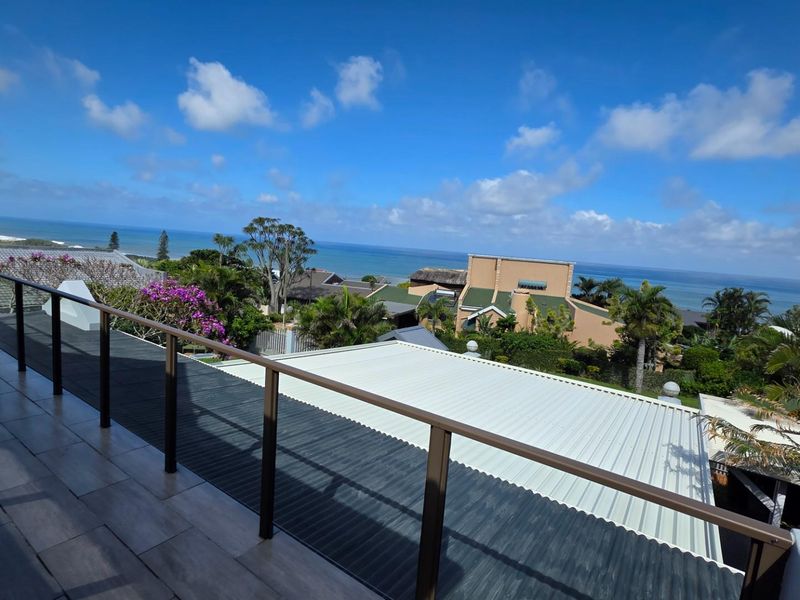 A spacious balcony featuring modern tiled flooring and a sleek metal railing, offering expansive elevated views of the surrounding coastal landscape.