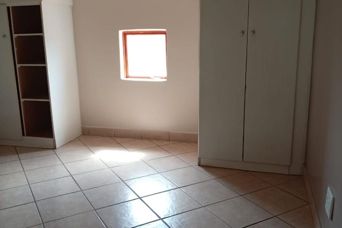 A bedroom featuring tiled flooring, built-in storage cabinetry, and a small window, providing a functional and neutral living space.