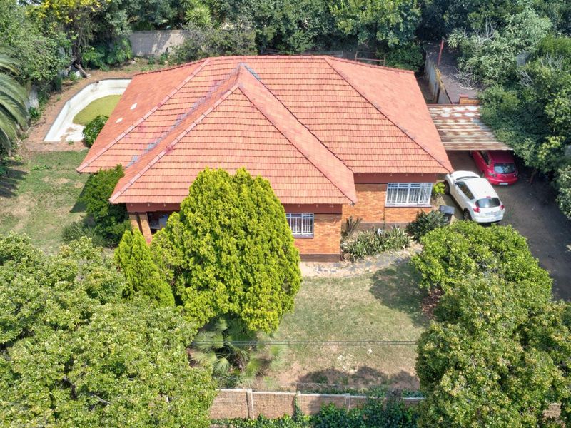 Aerial view of a detached brick house with a tiled roof, featuring a swimming pool, carport, and established garden on the property.