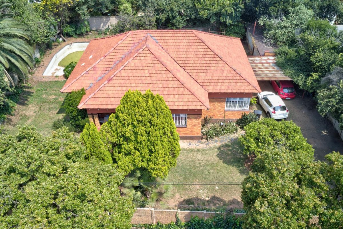 Aerial view of a detached brick house with a tiled roof, featuring a swimming pool, carport, and established garden on the property.