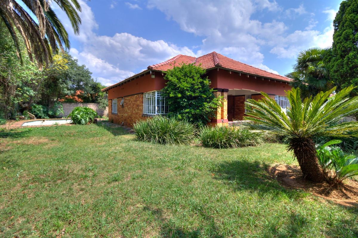 Rear view of a brick house featuring a terracotta tiled roof, security bars on windows, a swimming pool, and an established garden.