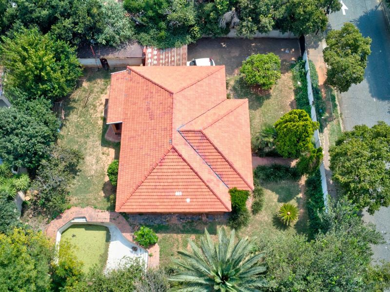 Aerial view of a residential property featuring a tiled roof, surrounding garden, and a swimming pool requiring maintenance.