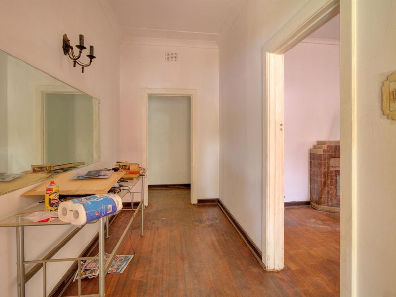 A hallway featuring original hardwood flooring, coved ceilings, and a large wall-mounted mirror, leading into adjacent living spaces with a tiled fireplace.