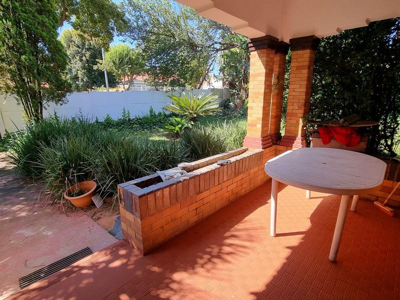 A covered outdoor patio featuring brick pillars and a built-in brick planter, overlooking a private garden area.